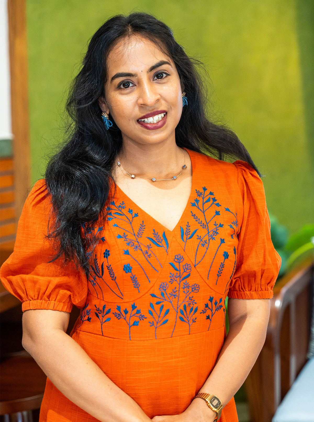 Blue floral embroidery across the yoke of an orange cotton dress, close-up - Ariyaa